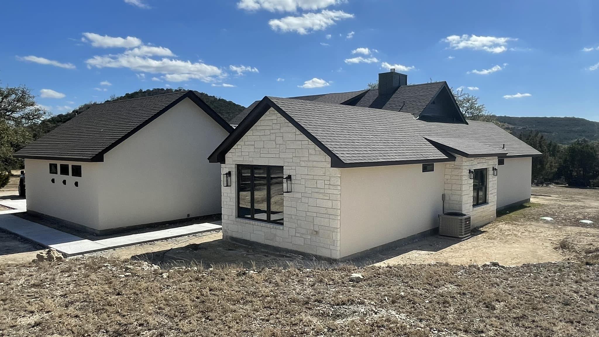 Contemporary home exterior showing off its unique design with a mix of stone and plaster finishes and asymmetrical roof lines against a clear blue sky.