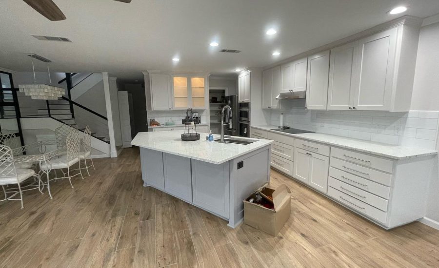 Interior view of a modern kitchen with white cabinetry, a large central island with gray base and white countertop, surrounded by a dining area with stylish black and white chairs.