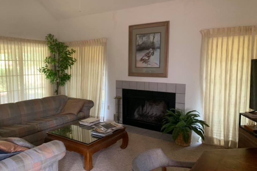 A classic living room setup with a large couch, traditional fireplace, and natural light streaming through large windows, offering a warm and inviting space.