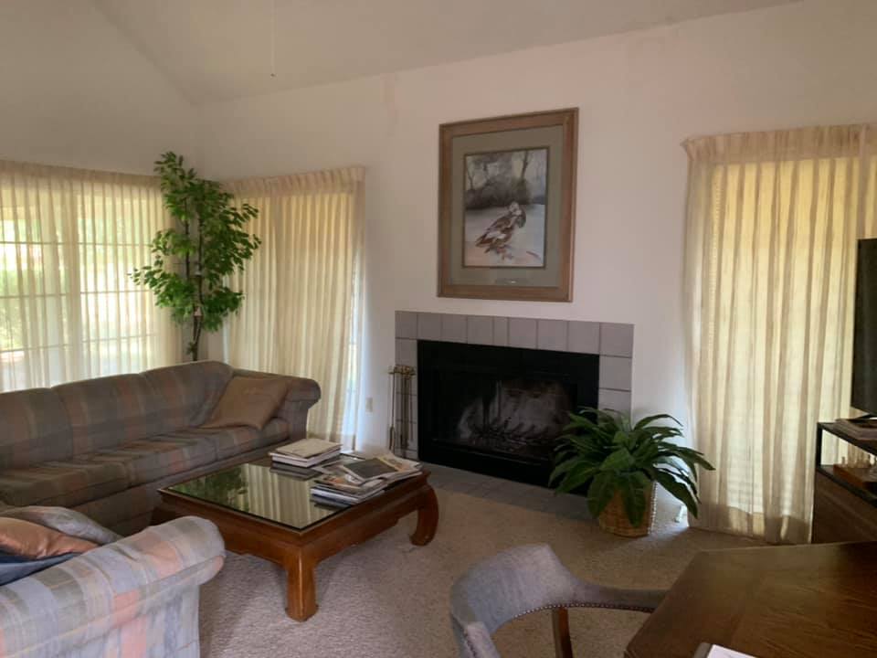 A classic living room setup with a large couch, traditional fireplace, and natural light streaming through large windows, offering a warm and inviting space.